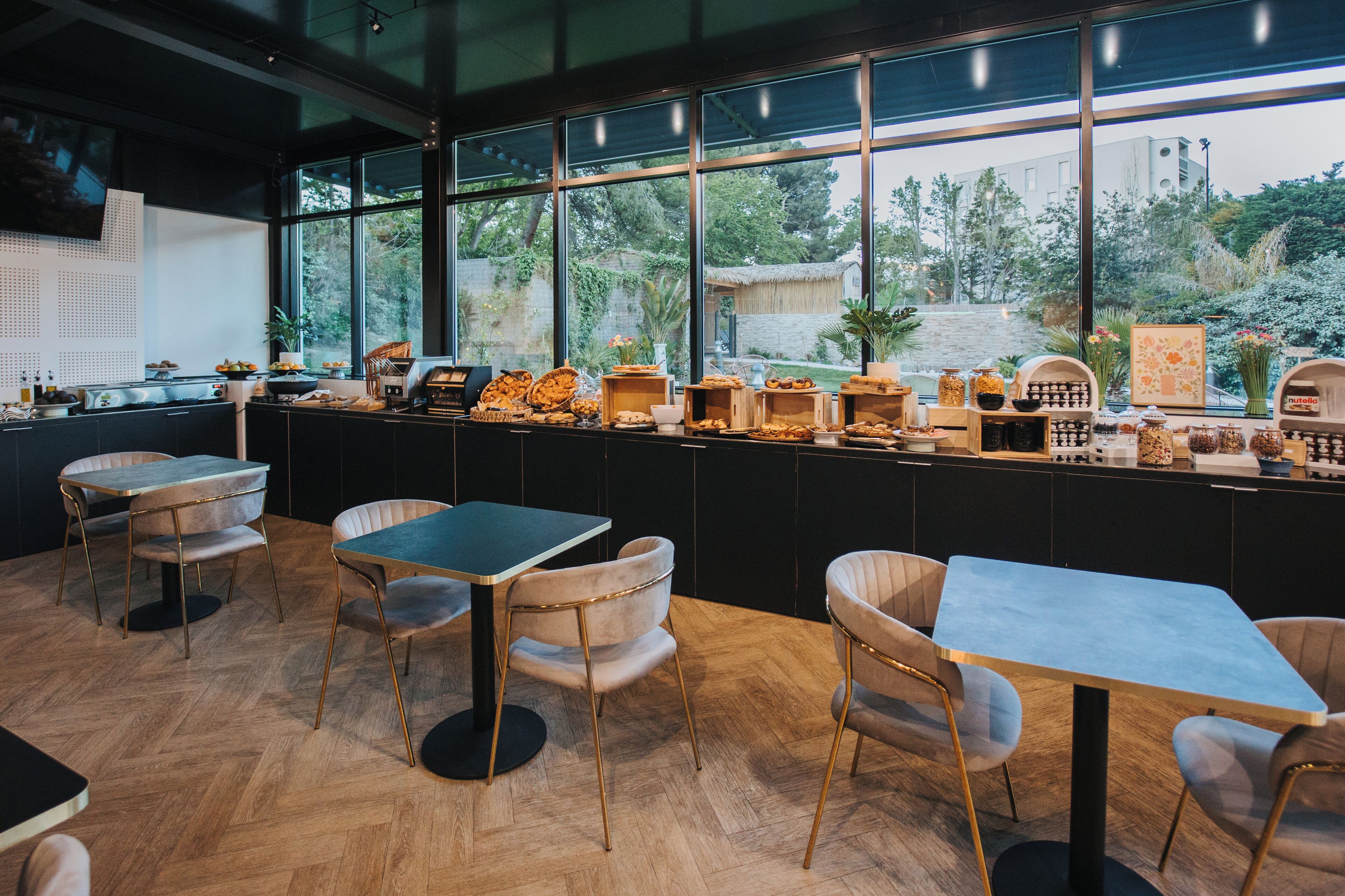 Restaurante moderno com balcão extenso, cadeiras de madeira e vista para o verde lá fora.