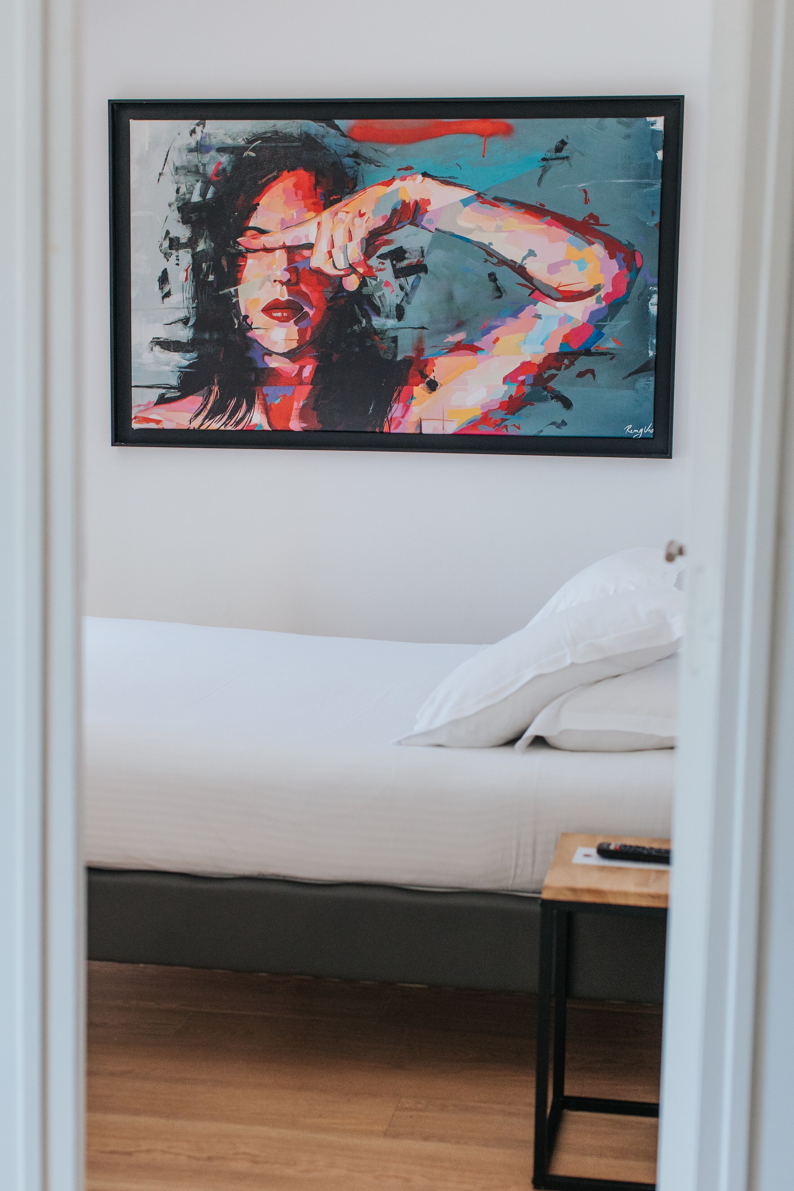A bedroom with a bed, a bedside table, and a framed artwork on the wall.