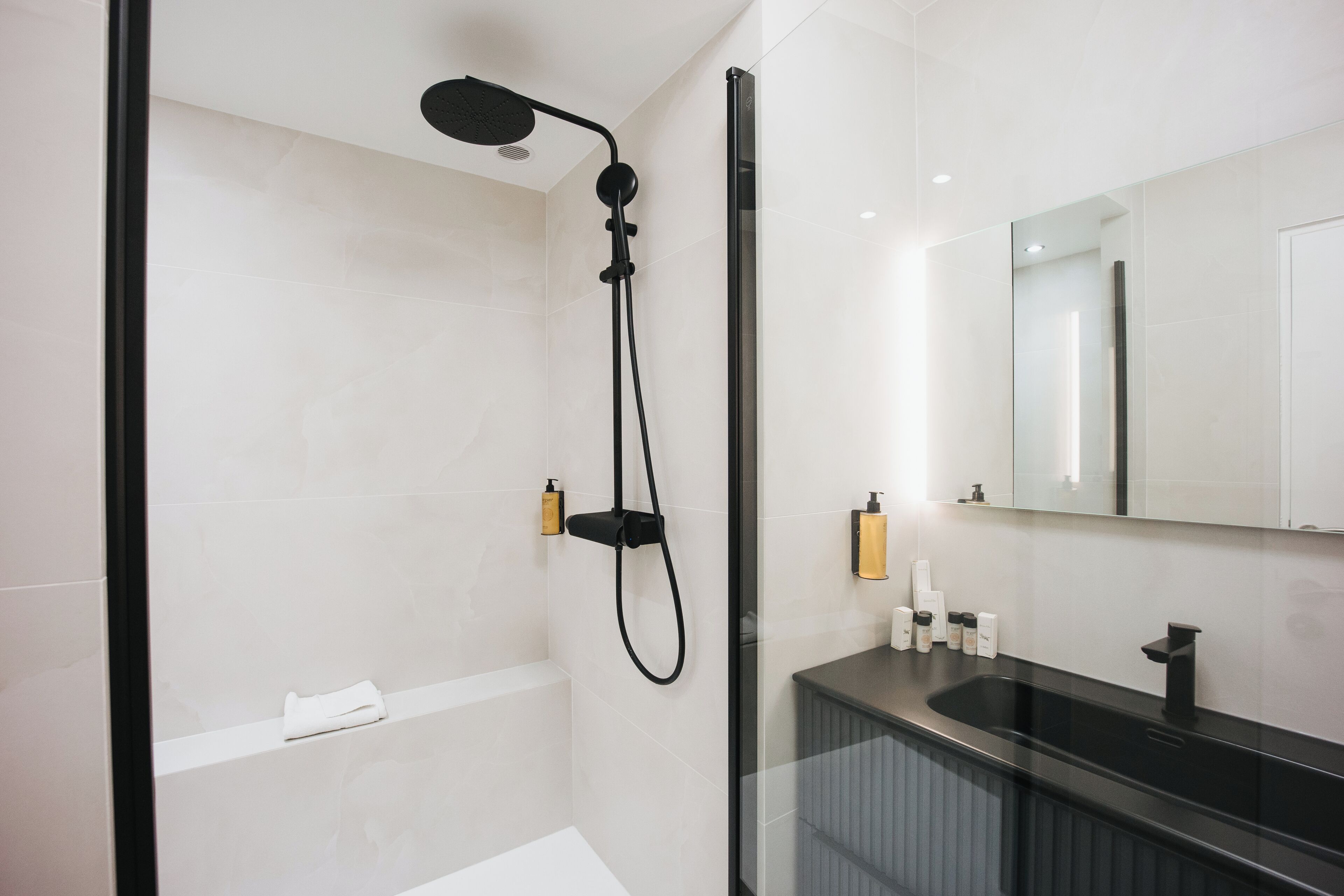 A modern bathroom with a glass shower enclosure, a black sink, and a large mirror.