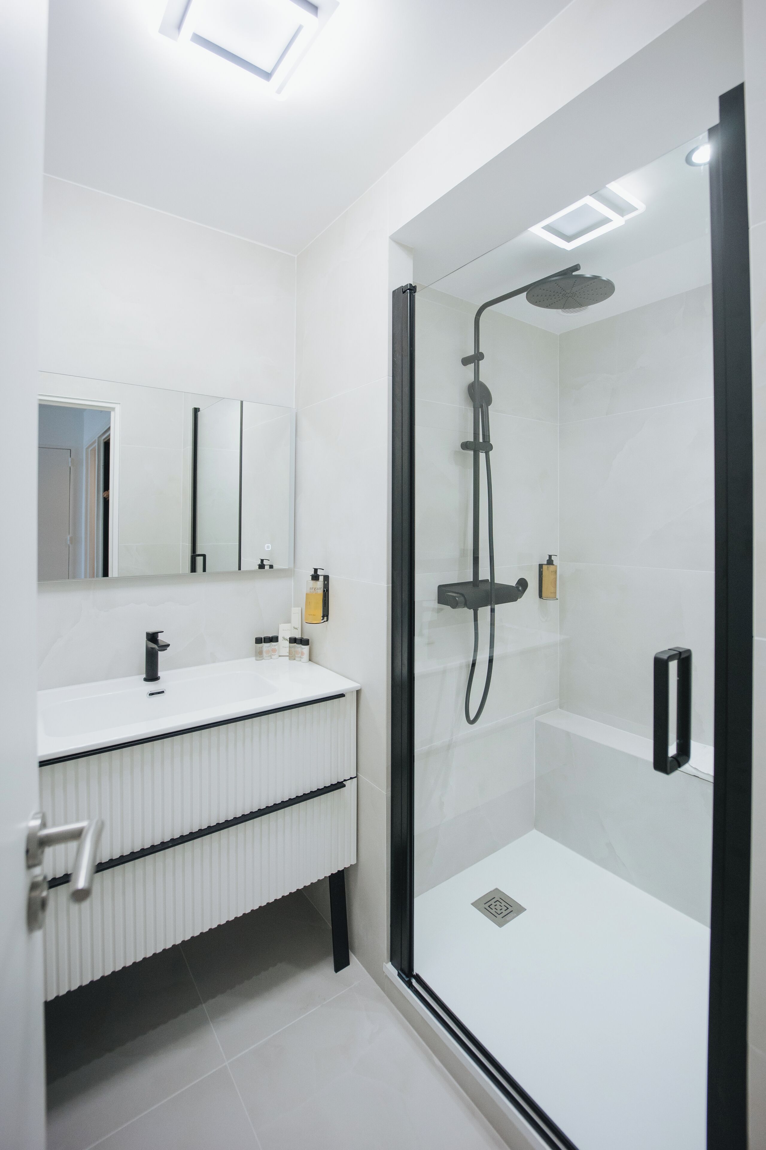 A modern bathroom with a glass-enclosed shower, a white vanity with a mirror, and a radiator under the sink.