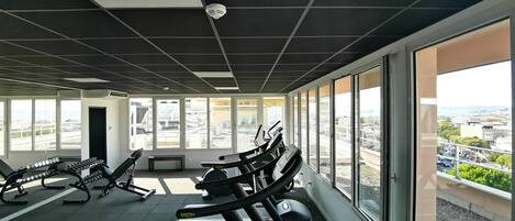 Un gimnasio con cintas de correr, mancuernas y máquinas de pesas, con amplias ventanas y vista a la ciudad.
