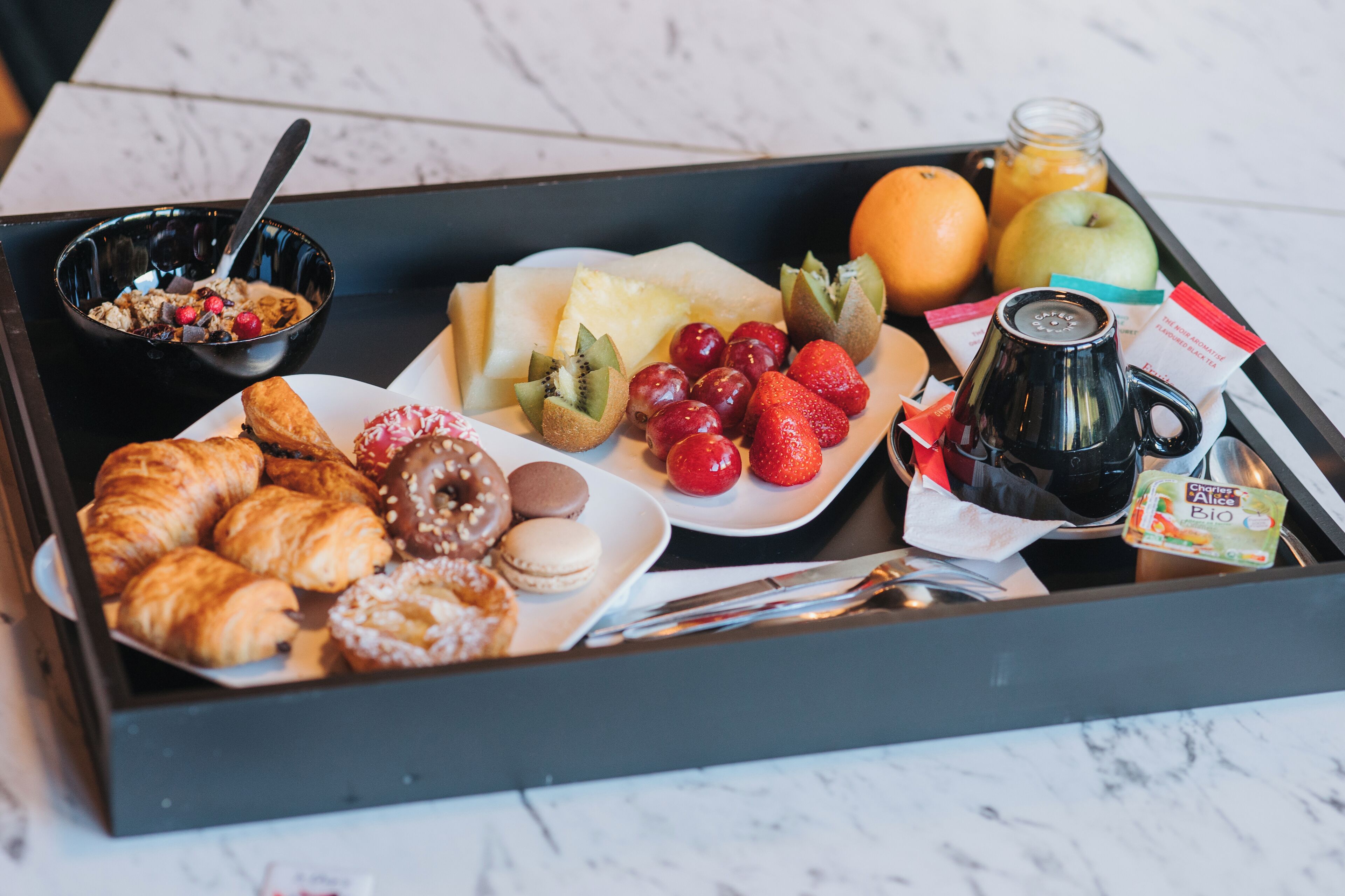 A breakfast tray with croissants, pastries, fruits, a coffee mug, and a bottle of juice.
