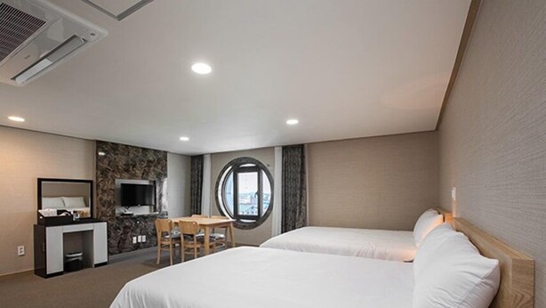 A hotel room with two beds, a desk, a TV, and a window with a view.