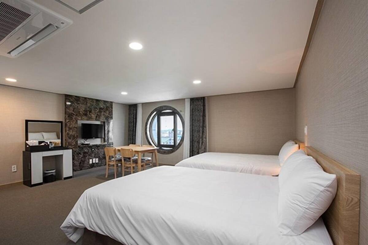 A hotel room with two beds, a desk, a TV, and a window with a view.