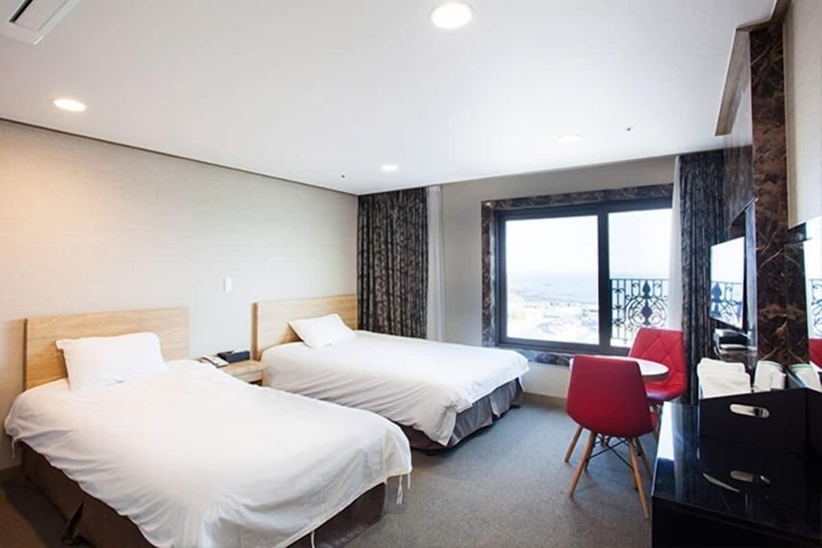 A hotel room with two beds, a desk, a chair, and a large window with a view.