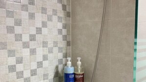 A shower with a checkered tile wall, a glass shelf with two bottles, and a handheld showerhead.