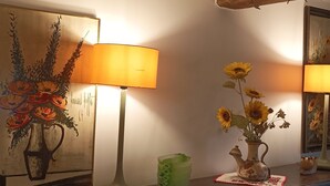 Een gezellige kamer met een houten tafel, een lamp, een vaas met zonnebloemen en een schilderij aan de muur.