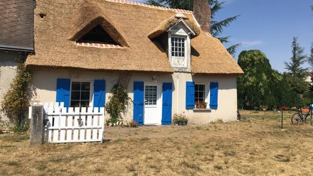 Een traditioneel huis met rieten dak, witte muren en blauwe luiken.