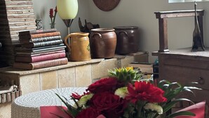 Een kamer met een rustieke bakstenen open haard, een verzameling hoeden aan de muur en een tafel met een bloemenboeket.
