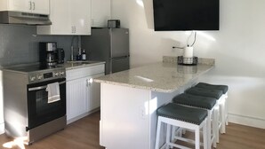 A modern kitchen with white cabinets, stainless steel appliances, a granite countertop, and a black TV mounted on the wall.