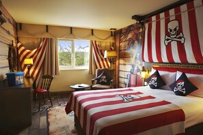 Une chambre avec un lit agrémenté d’une couvre-lit sur le thème des pirates, de rideaux à rayures et d’une décoration murale représentant un crâne et des os croisés.
