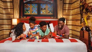 A room with a wooden wall, a bed with red and white bedding, and a window with a view of the outside. - Legoland Hotel (Carlsbad)