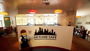 A LEGO figure standing in front of a sign for Skyline Café, with a bar area and seating visible in the background. - Legoland Hotel (Carlsbad)