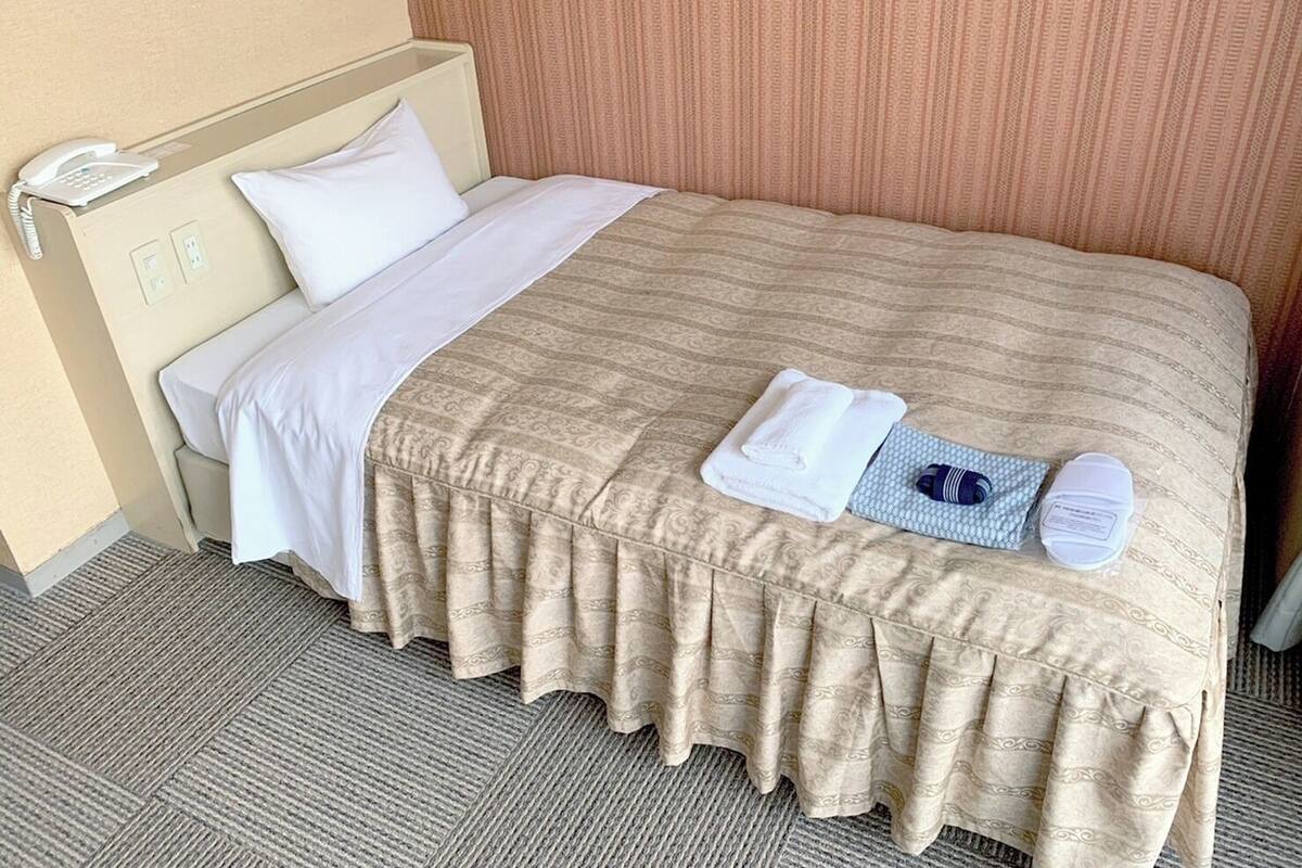 A neatly made hotel bed with a white and beige bedspread, a white pillow, and a folded towel on the bed.