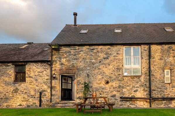 A stone building with a pitched roof, a front door, and a small table with a plant.