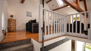 A spacious living area with a staircase, wooden flooring, a sofa, a lamp, and a painting on the wall. - Hill Top 1: 3-Bed Cottage in Caergeiliog | Managed by Anglesey Holiday Lettings (Caergeiliog)