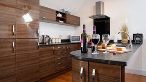 A modern kitchen with wooden cabinets, a built-in wine rack, and a countertop with wine glasses and a cutting board. - Hill Top 1: 3-Bed Cottage in Caergeiliog | Managed by Anglesey Holiday Lettings (Caergeiliog)