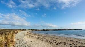 Une plage côtière bordée de galets, avec des rochers escarpés visibles au loin et un ciel dégagé.