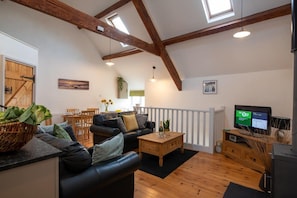 A spacious living room with a wooden ceiling, a black leather sofa, a wooden coffee table, and a television.