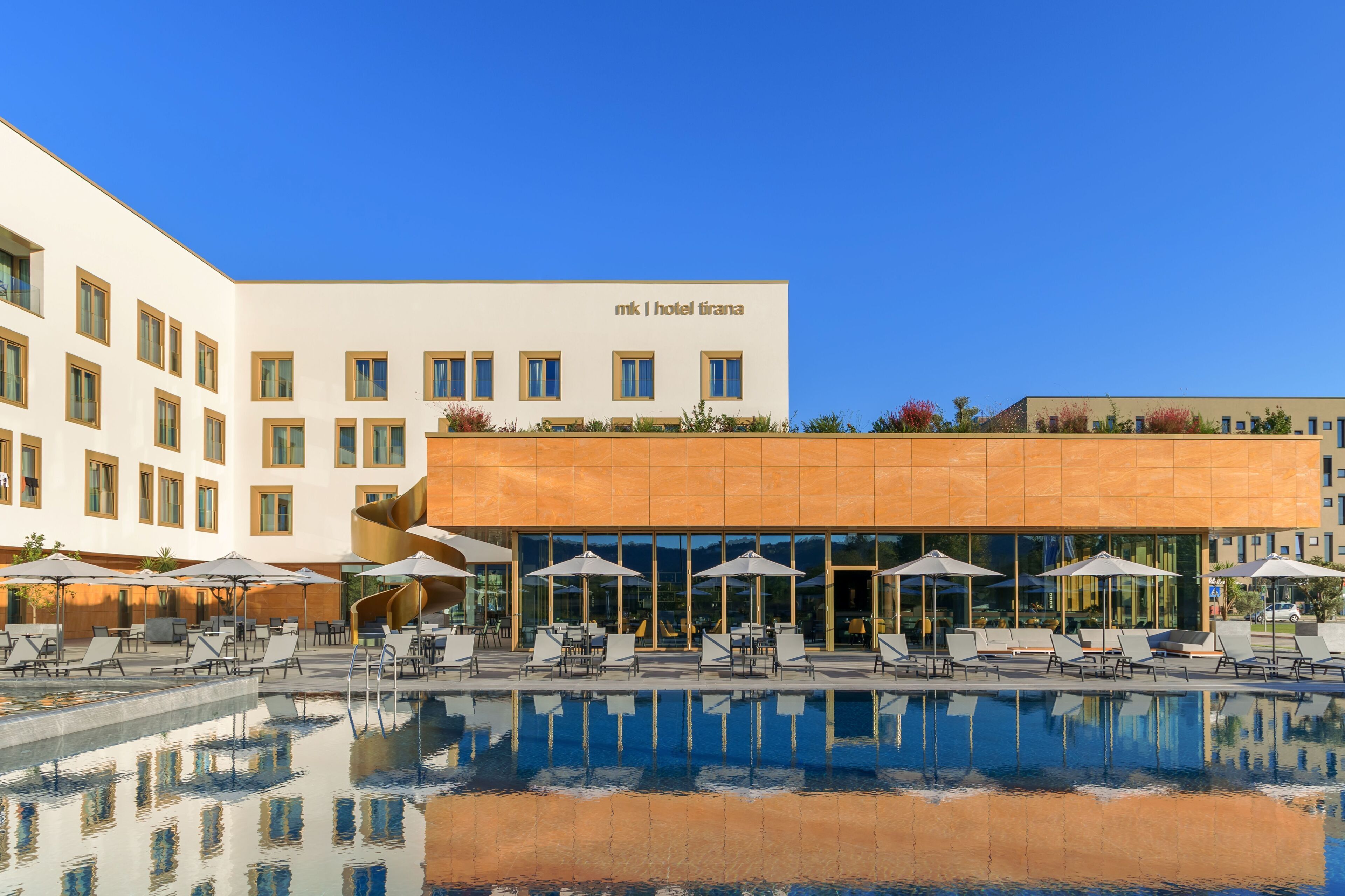 A hotel with a pool, sun loungers, and umbrellas.