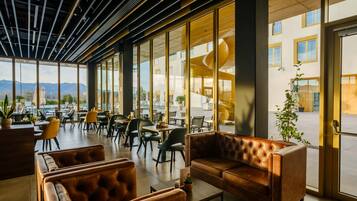 A modern interior with leather sofas, a dining area, and large windows offering a view of the outdoors.