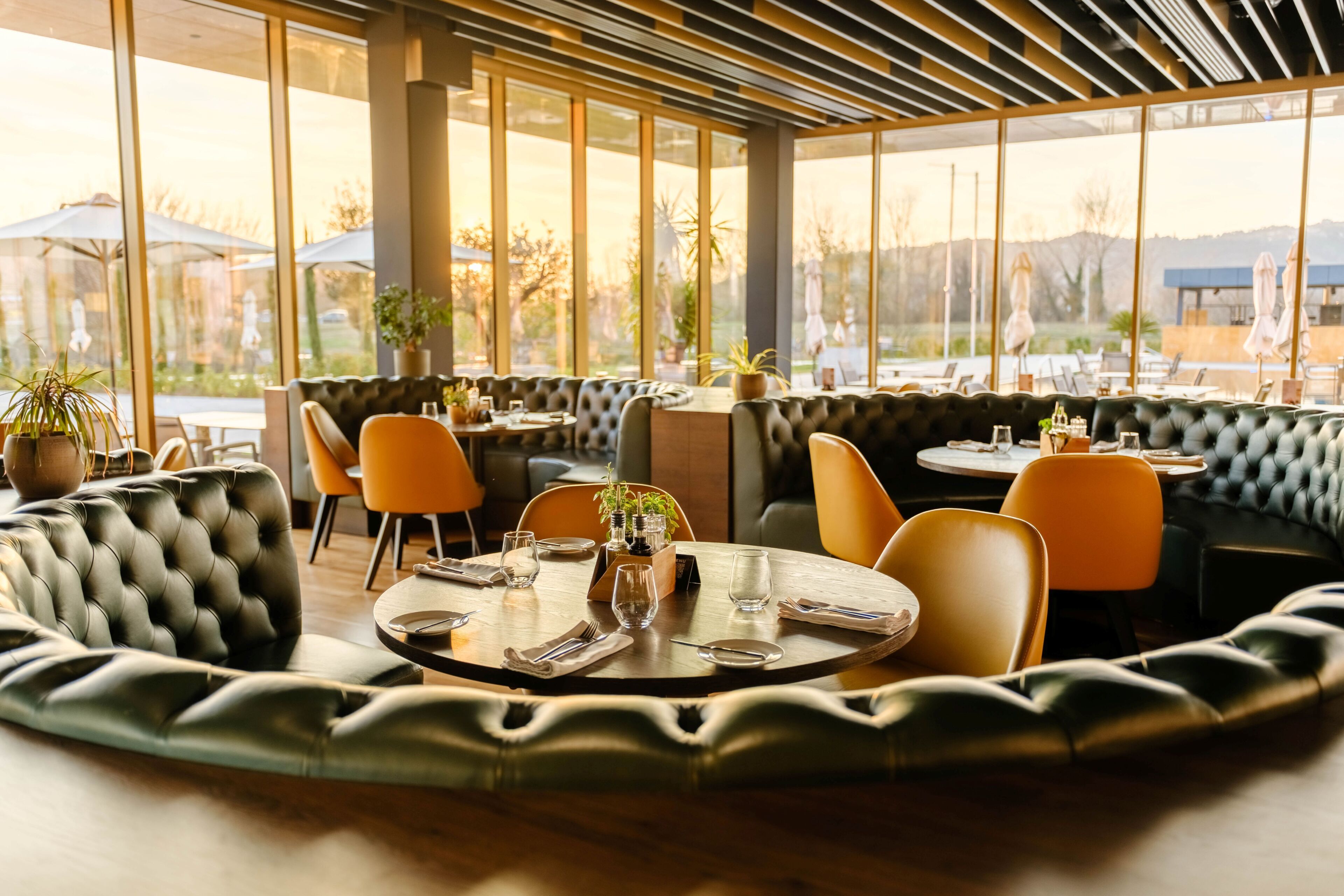 A restaurant with round tables, cushioned seating, and large windows.