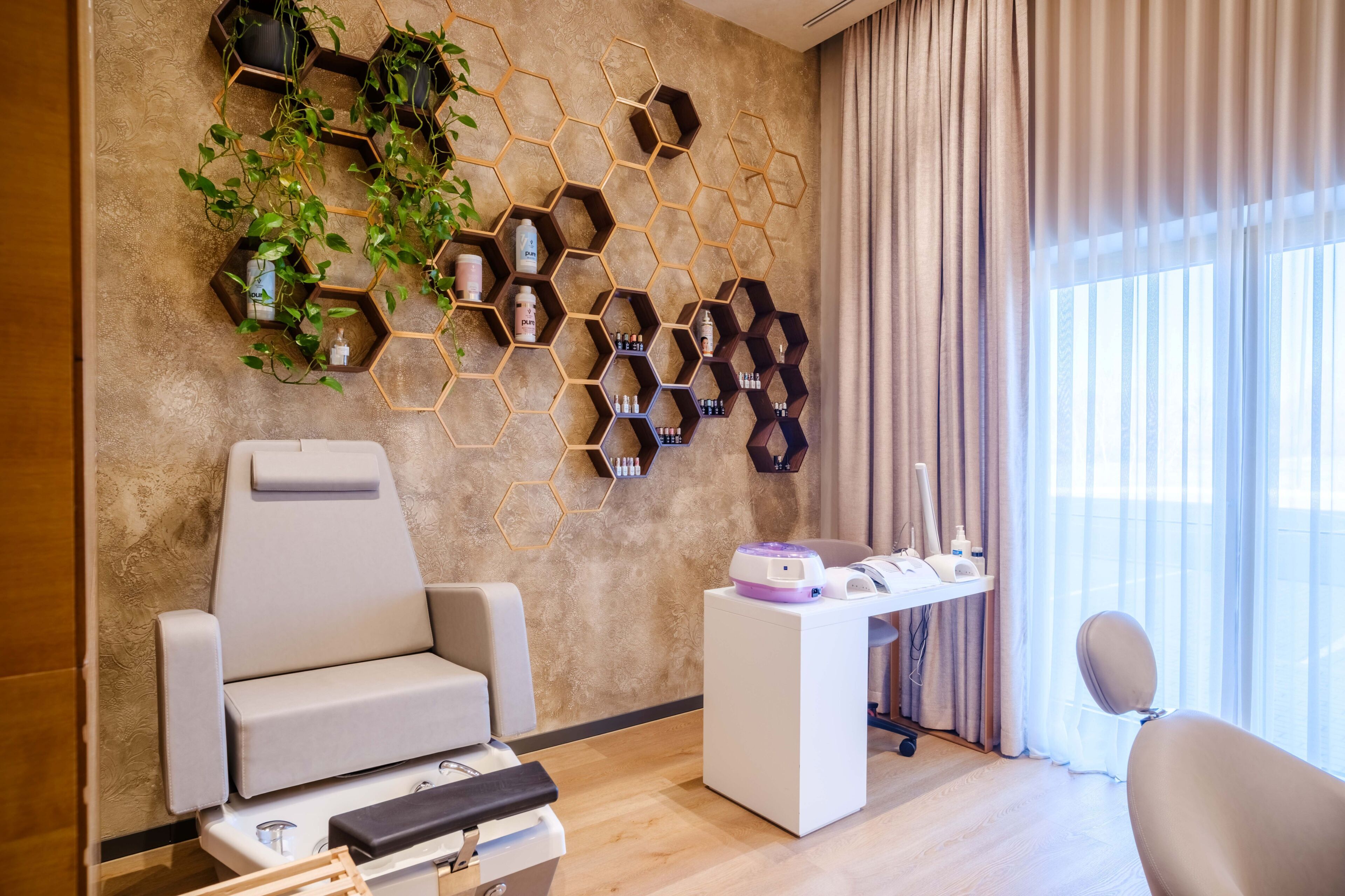 Ein modernes Zimmer mit Massage-Sessel, einem kleinen Schreibtisch mit Massagegerät und einem sechseckigen Wandregal mit Pflanzen und Flaschen.
