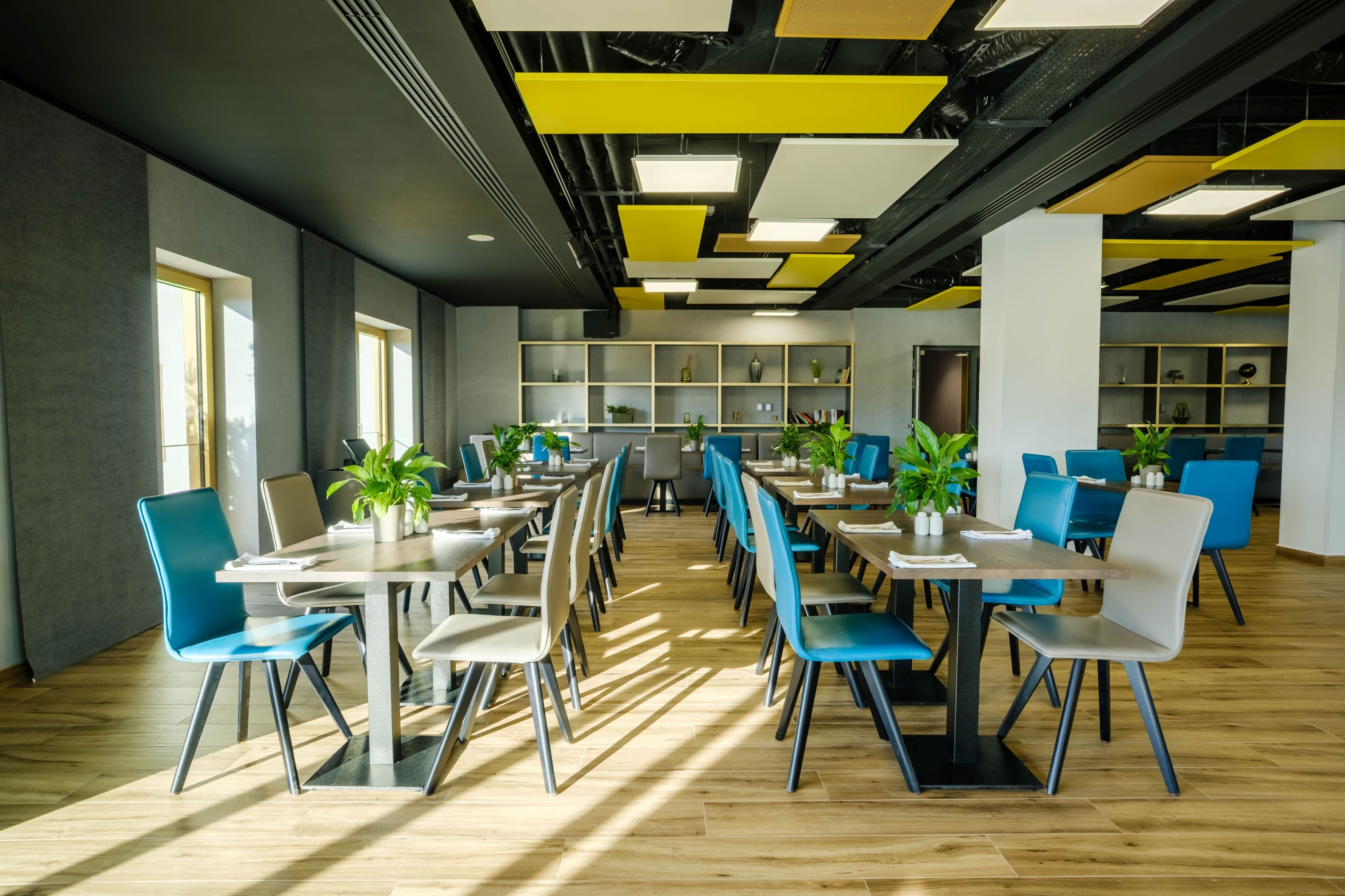A modern dining area with tables and chairs, potted plants, and a wooden floor.