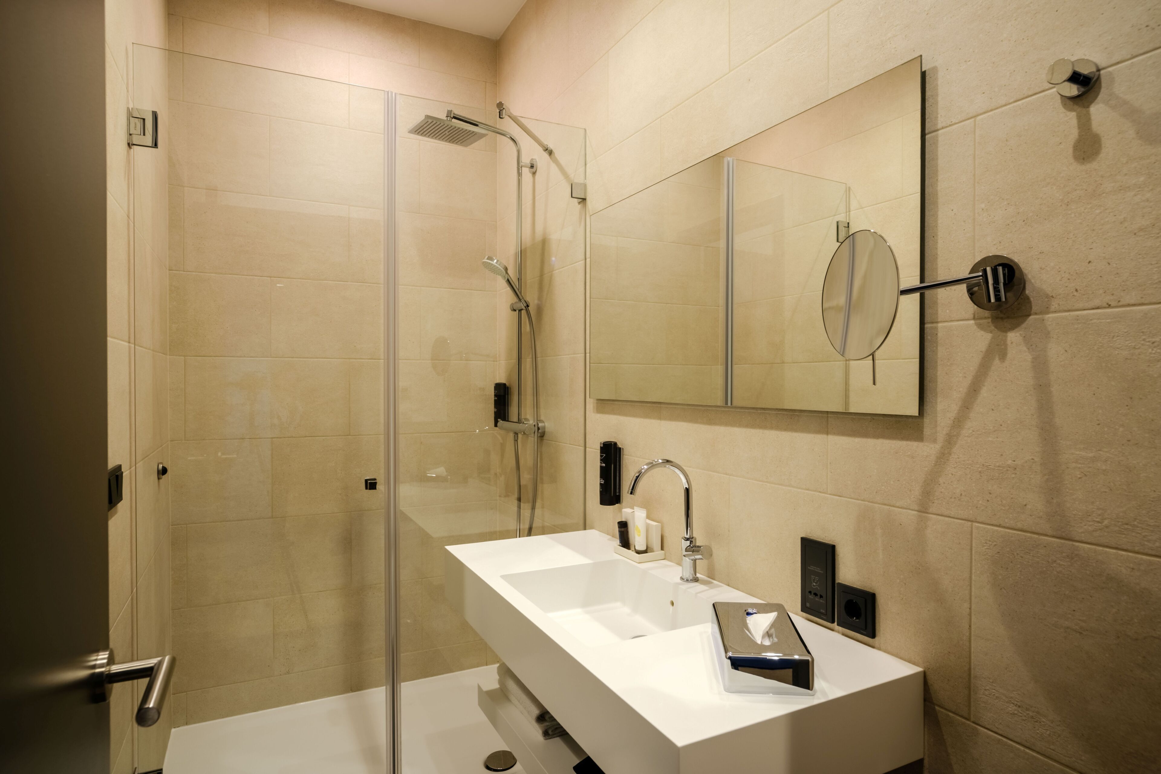 A modern bathroom with a glass-enclosed shower, a white sink, and a large mirror.