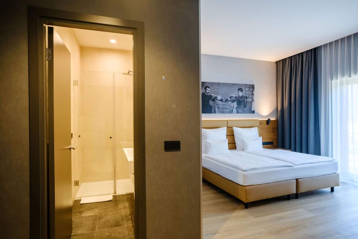 A hotel room with a bed, a shower, a door, and a wall-mounted picture.