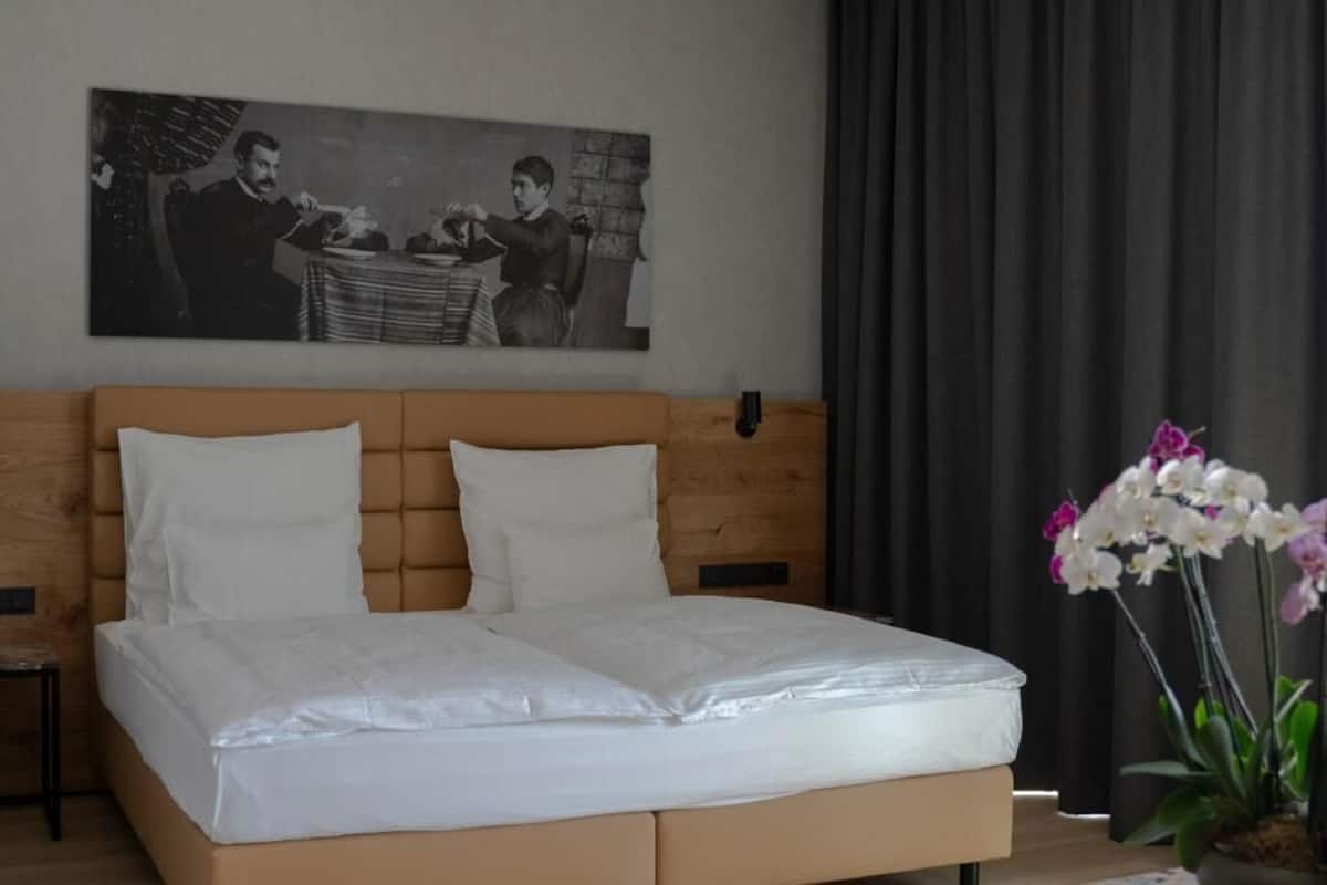 A bed with white linens, a wooden headboard, and a black and white photograph above it.
