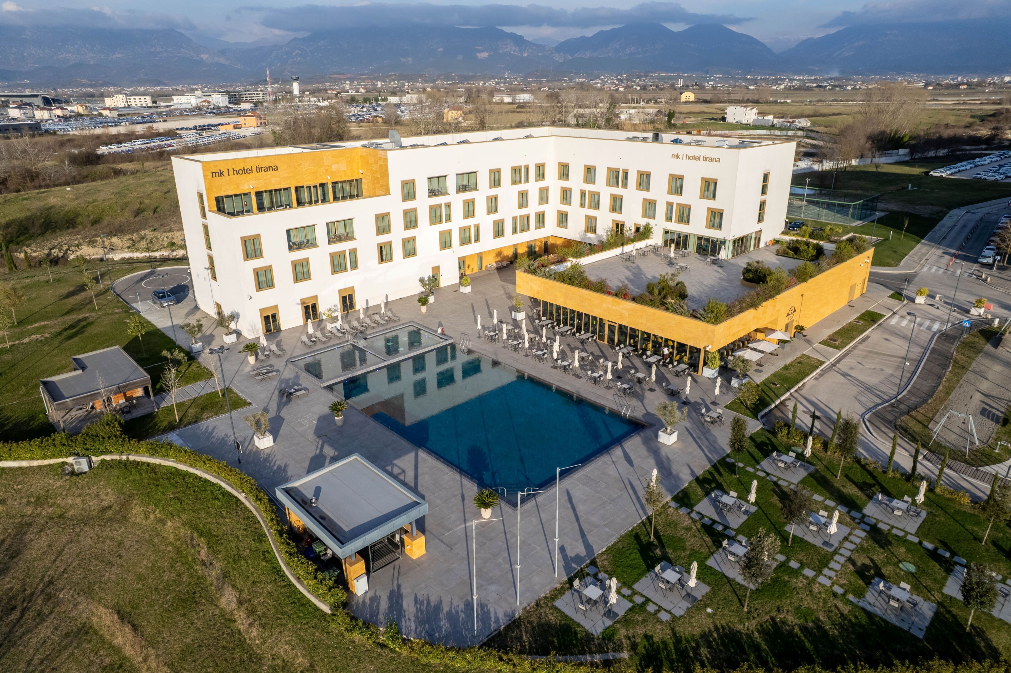 A hotel with a large pool, multiple balconies, and a parking area.
