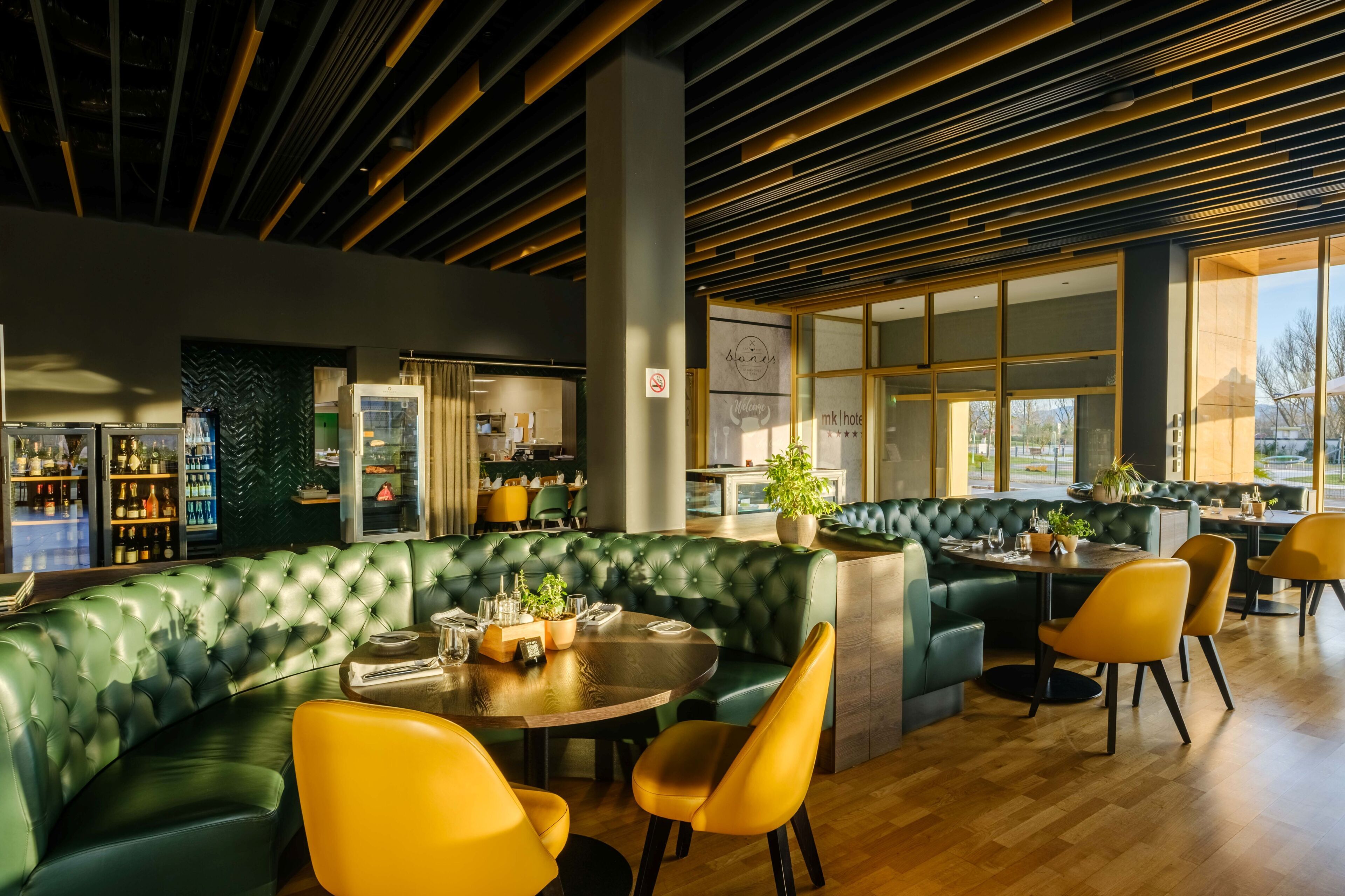 Een modern restaurant met groen bekleden zitplaatsen, gele stoelen en een houten plafond.
