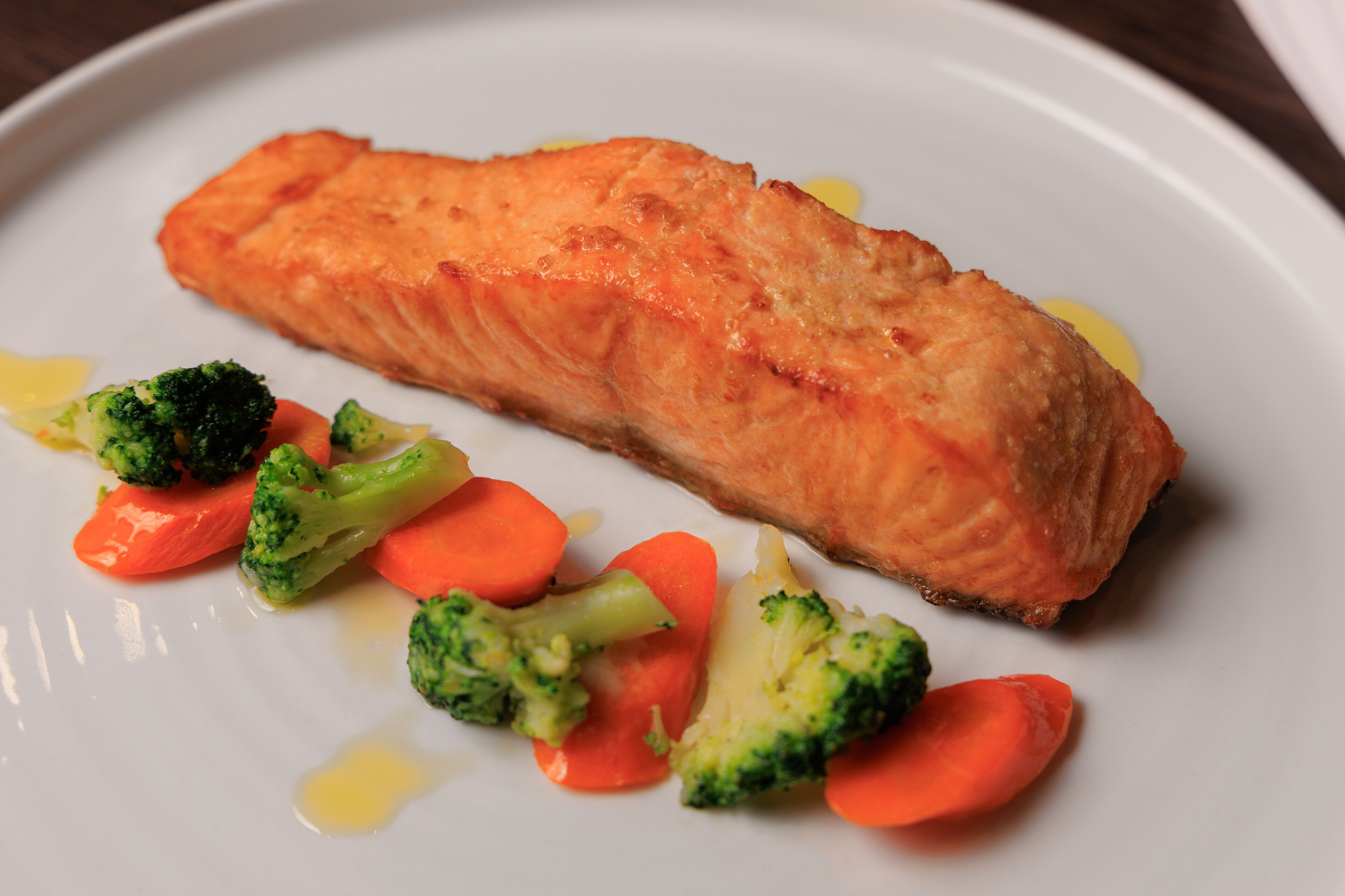 Een bord met zalm, broccoli en wortels.