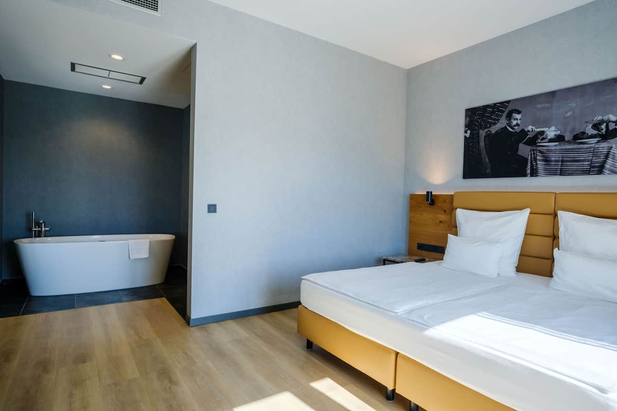 A modern bedroom with a large bed, a bathtub, and a painting on the wall.