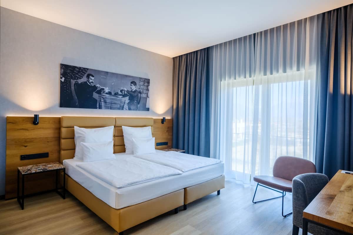 A hotel room with a large bed, a small table, a chair, and a painting on the wall.