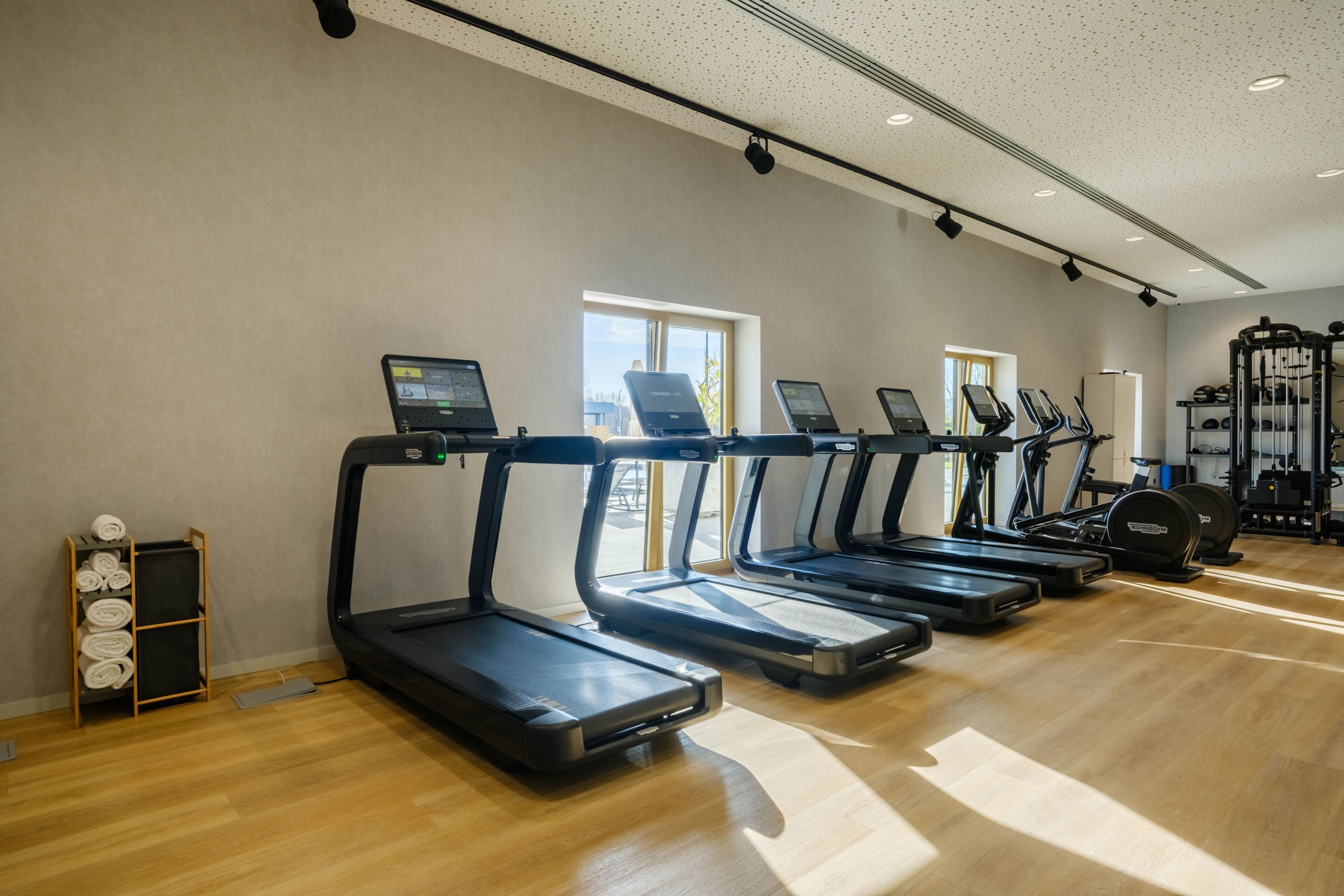 Un gimnasio con cintas de correr, máquinas de pesas y suelo de madera.