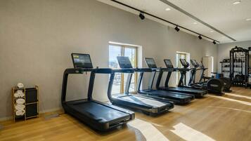 Un gimnasio con cintas de correr, máquinas de pesas y suelo de madera.