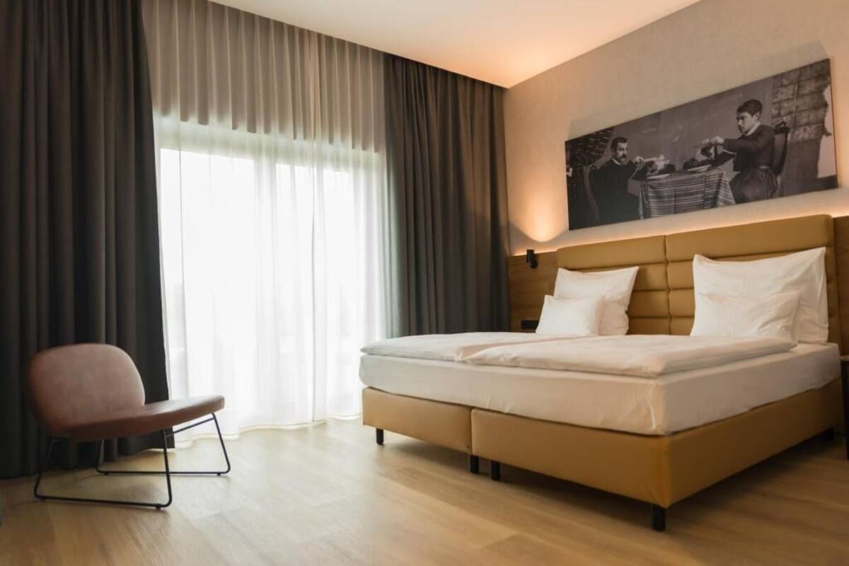 A modern hotel room with a large bed, a chair, and a painting on the wall.