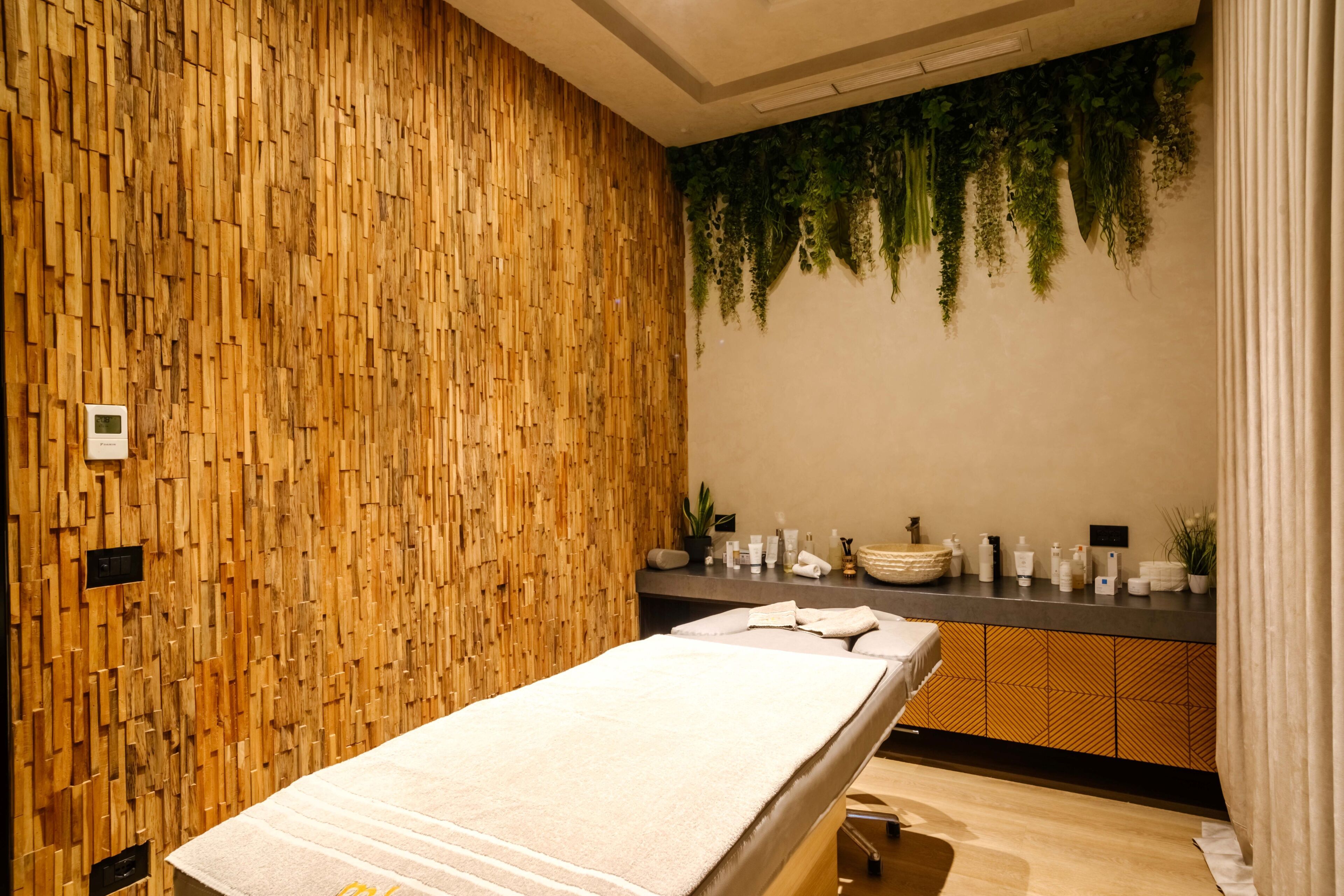 Una habitación con pared de madera, un mostrador de recepción, una camilla de masaje y una planta colgada en la pared.