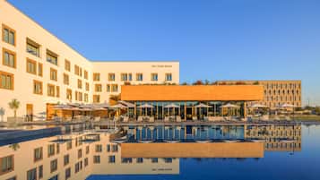 A hotel with a swimming pool, outdoor seating, and a clear sky.
