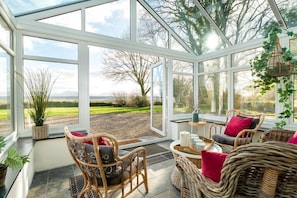 A conservatory with wicker furniture, a view of the outdoors, and a hanging plant. - Ty Fferam Bailey: A beautiful 7 bed holiday home in Anglesey (Bodorgan)