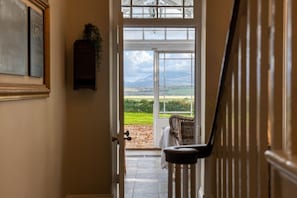 A hallway leading to a glass door with a view of a green landscape and mountains. - Ty Fferam Bailey: A beautiful 7 bed holiday home in Anglesey (Bodorgan)