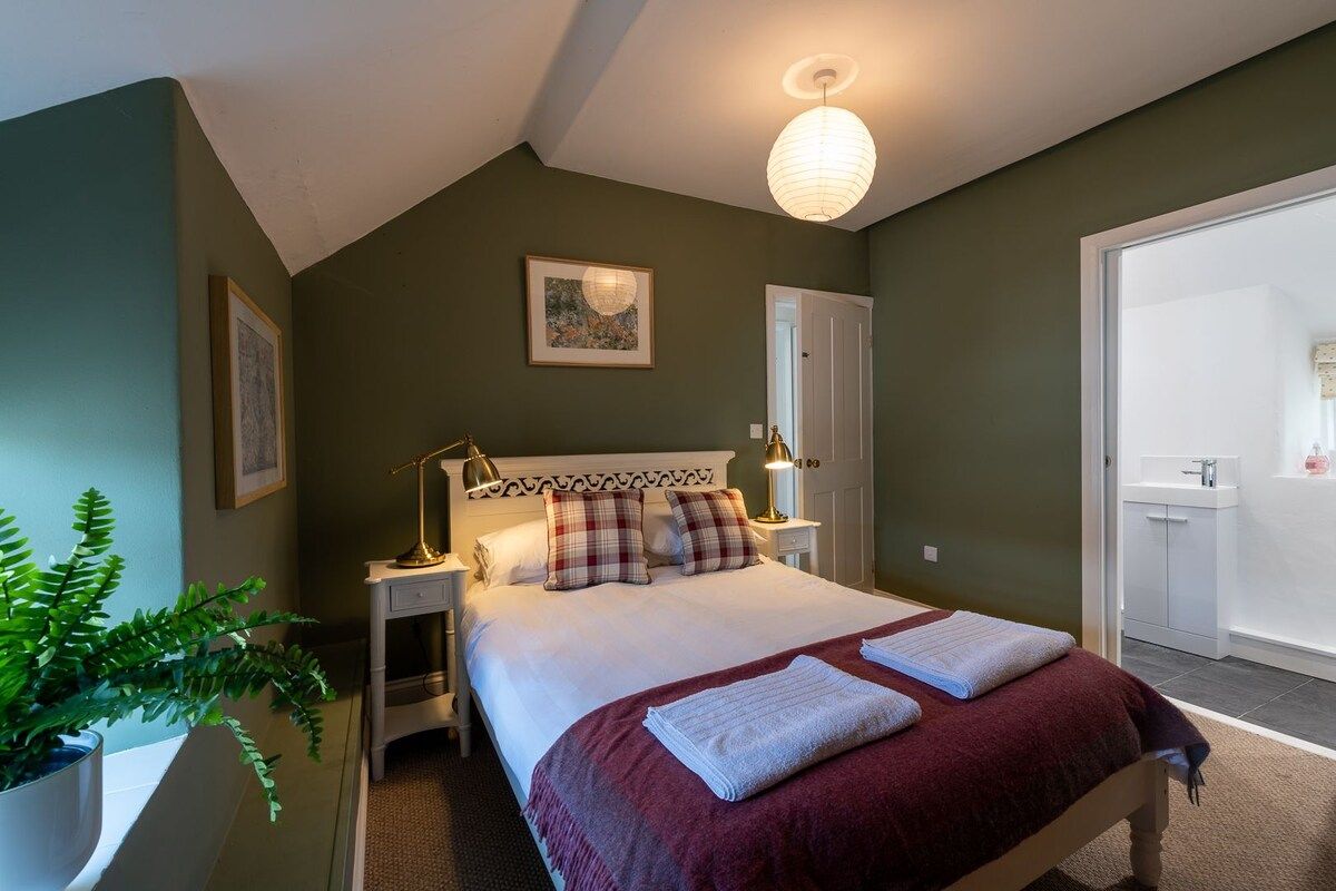 Une chambre à coucher comprenant un lit, des tables de chevet, une commode, une plante en pot et une porte donnant sur une salle de bain.