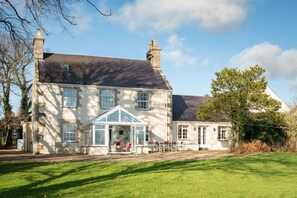 A large two-story house with a conservatory, a lawn, and a clear sky. - Ty Fferam Bailey: A beautiful 7 bed holiday home in Anglesey (Bodorgan)