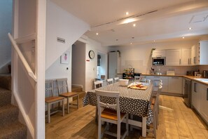 A modern kitchen with white cabinetry, a dining table with a polka dot tablecloth, and a staircase leading to another room. - Ty Fferam Bailey: A beautiful 7 bed holiday home in Anglesey (Bodorgan)