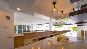 A modern kitchen with a marble countertop, wooden bench seating, pendant lighting, and a view of the outdoors. - Cozy 3 Bedroom Pool Villa L70 (Hua Hin)