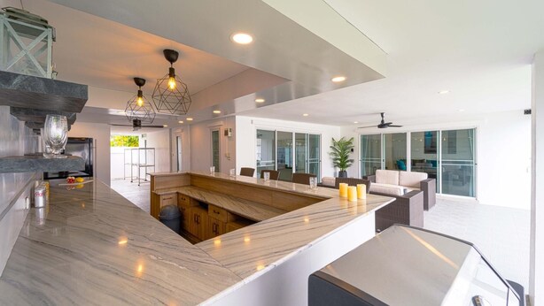 A modern kitchen with a marble countertop, wooden cabinets, and a central island. - Cozy 3 Bedroom Pool Villa L70 (Hua Hin)