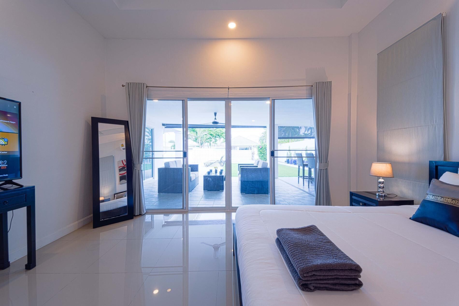 A hotel room with a bed, a TV, a lamp, and a sliding glass door leading to an outdoor seating area.