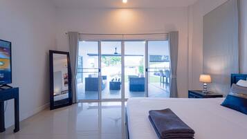 A hotel room with a bed, a TV, a lamp, and a sliding glass door leading to an outdoor seating area.